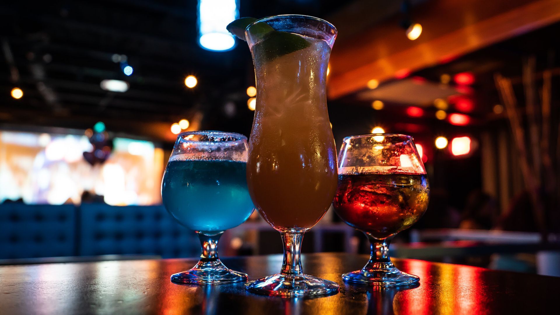 Three drinks are sitting on a table in a dark room.