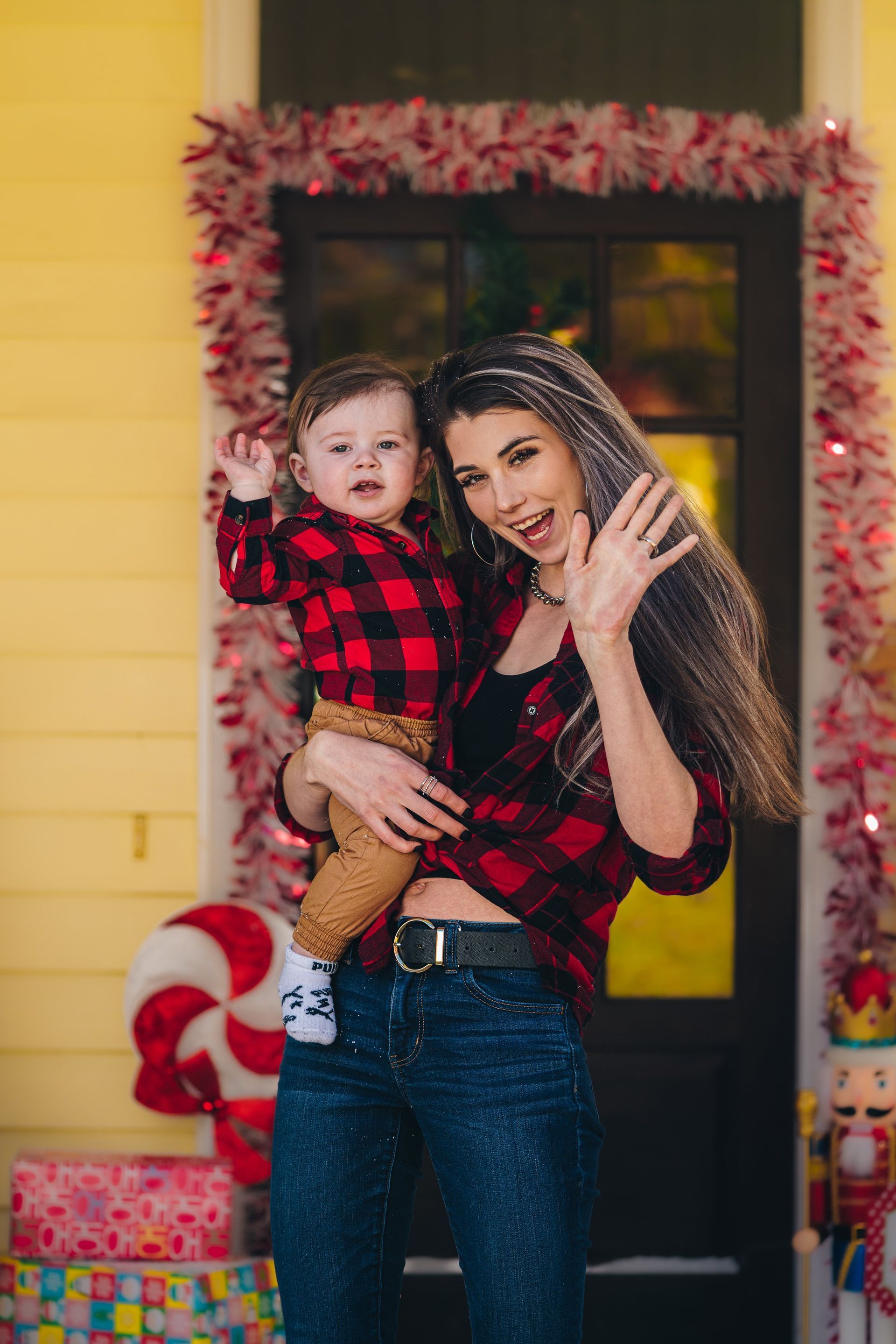 A woman is holding a baby in her arms in front of a house decorated for christmas.