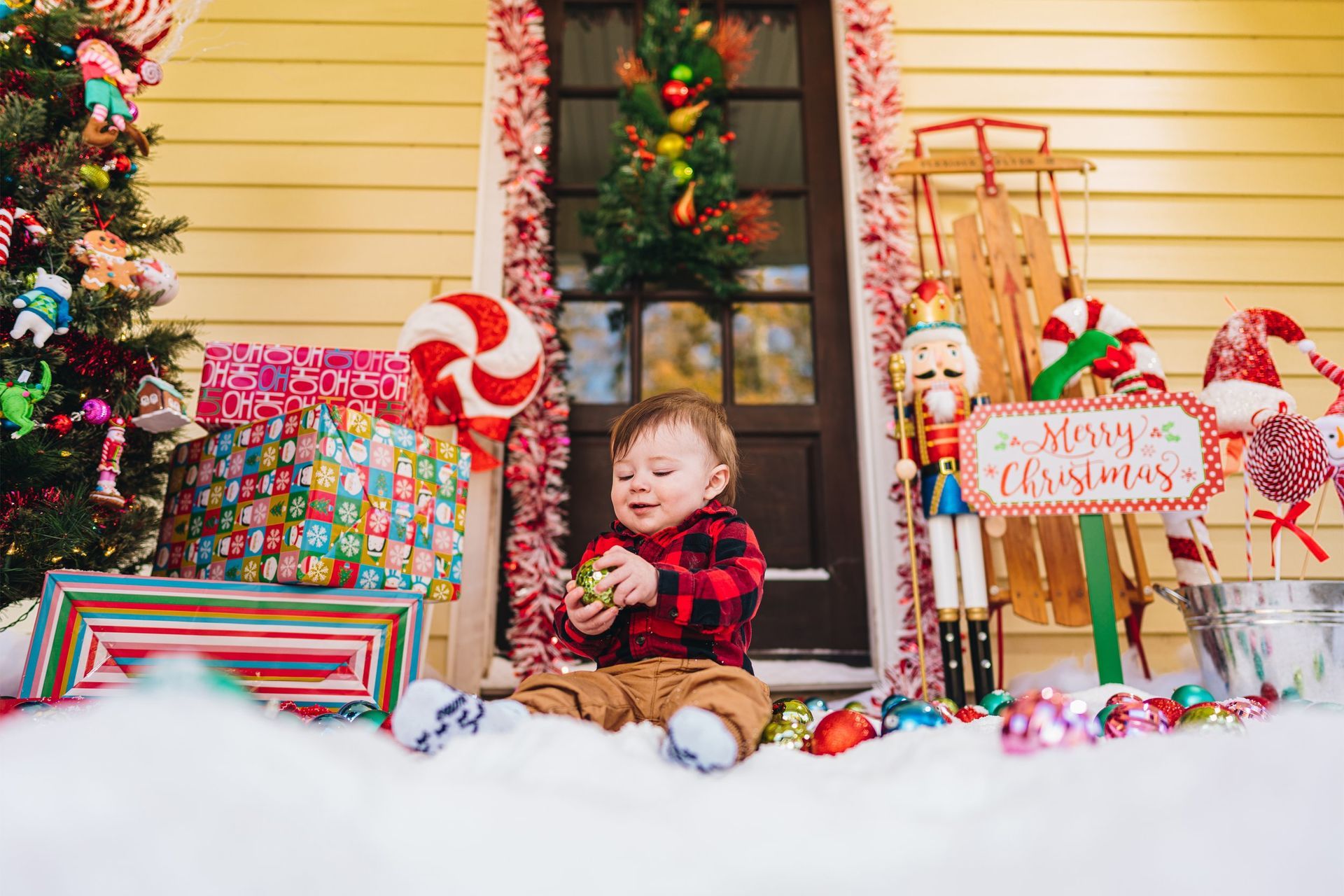 A baby is sitting on a porch decorated for christmas.