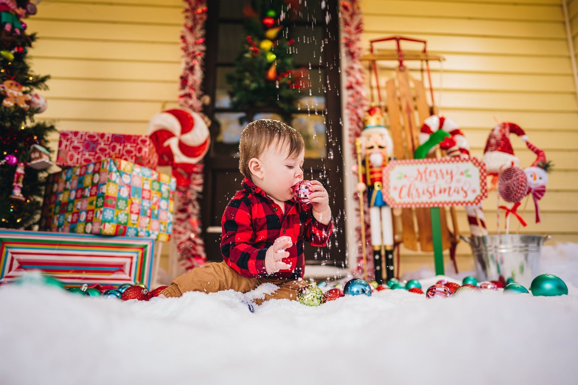 A baby is laying in the snow eating a candy cane.