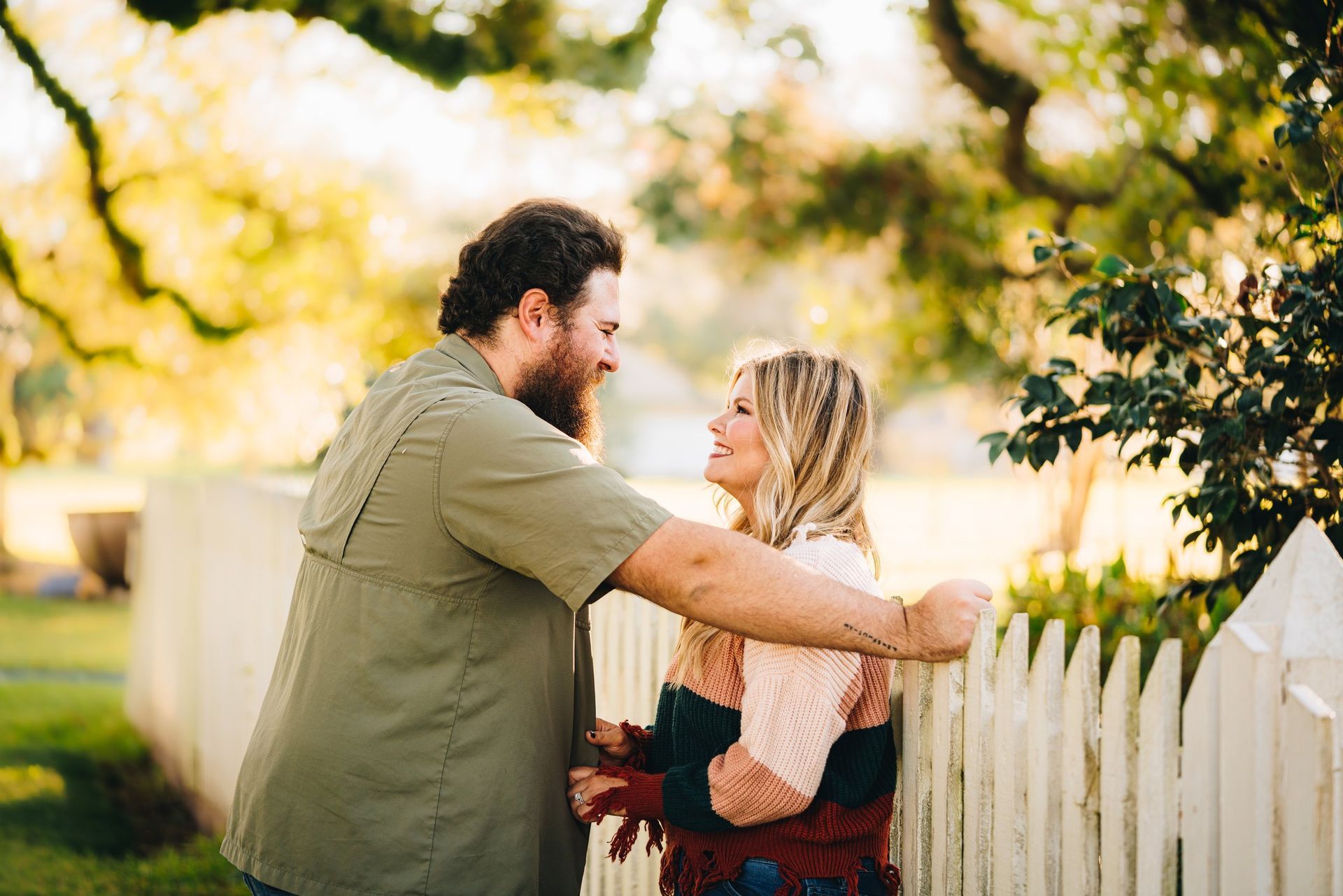 A man and a woman are hugging each other while standing next to a white picket fence.