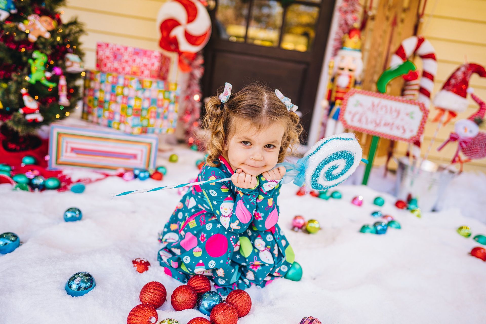 A little girl is sitting in the snow surrounded by christmas decorations.