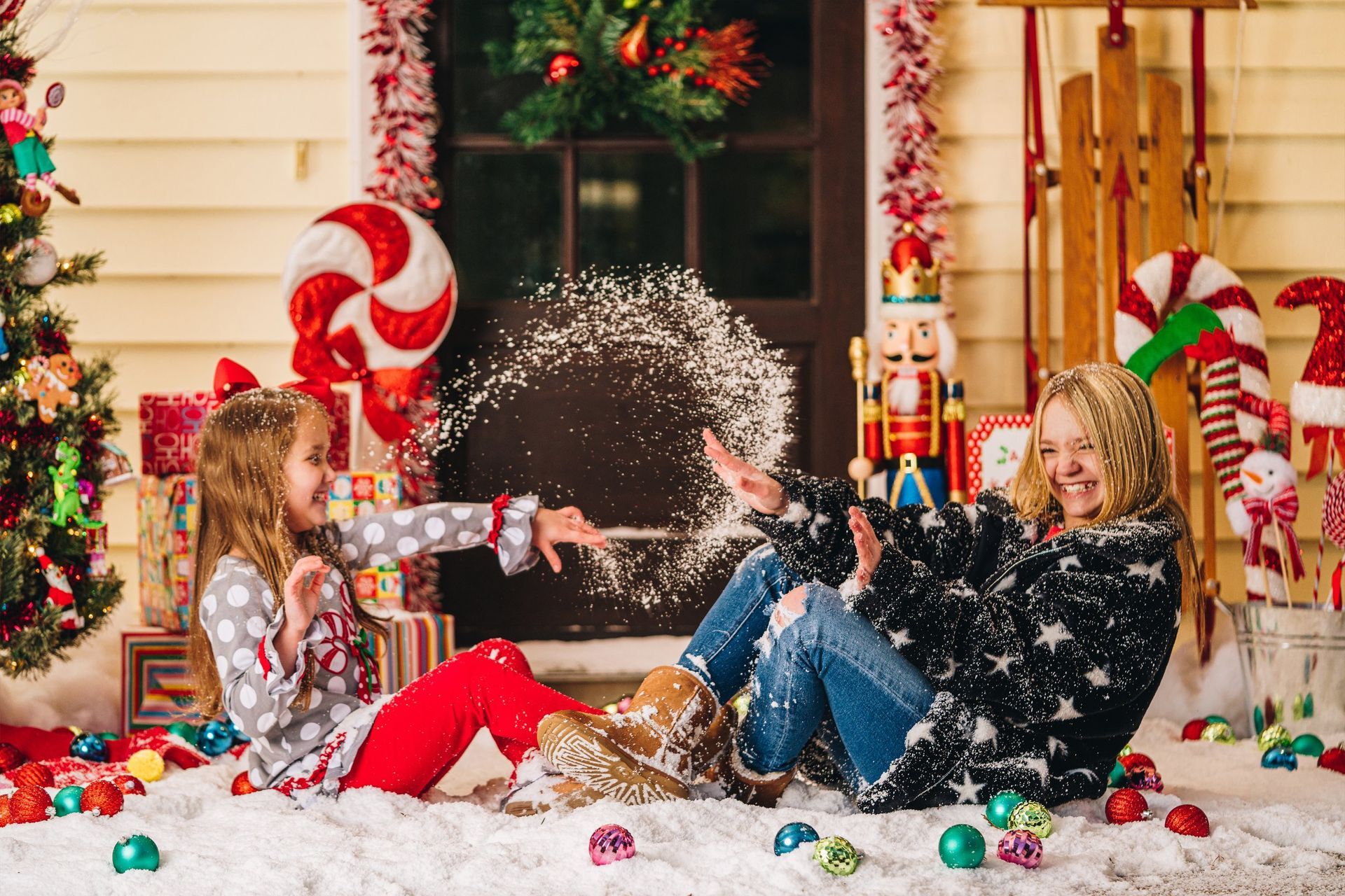 A mother and daughter are playing in the snow on a porch decorated for christmas.