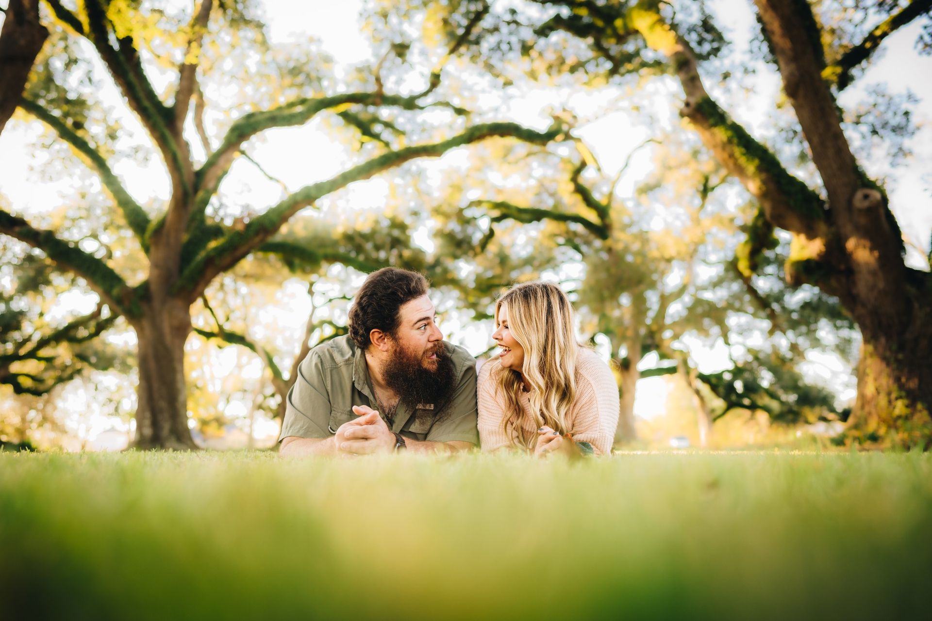 A man and a woman are laying in the grass under a tree.