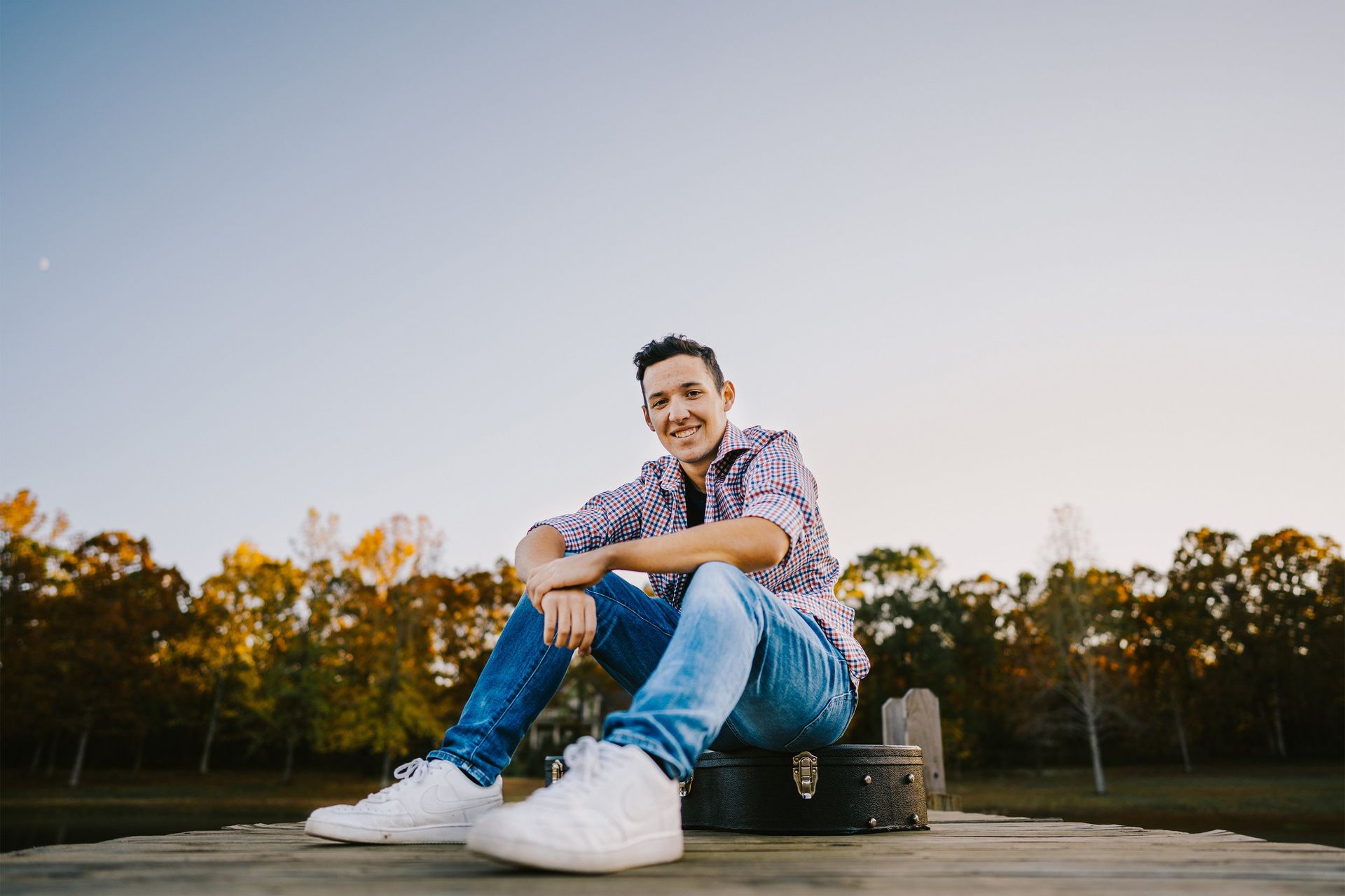 A young man is sitting on a dock with a guitar case.