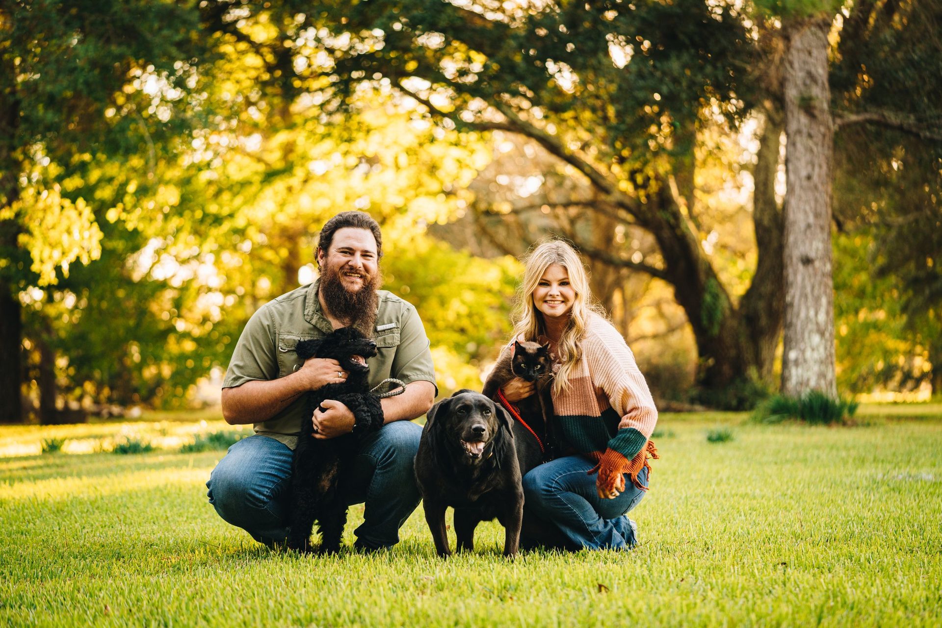 A man and a woman are posing for a picture with their dogs in a park.