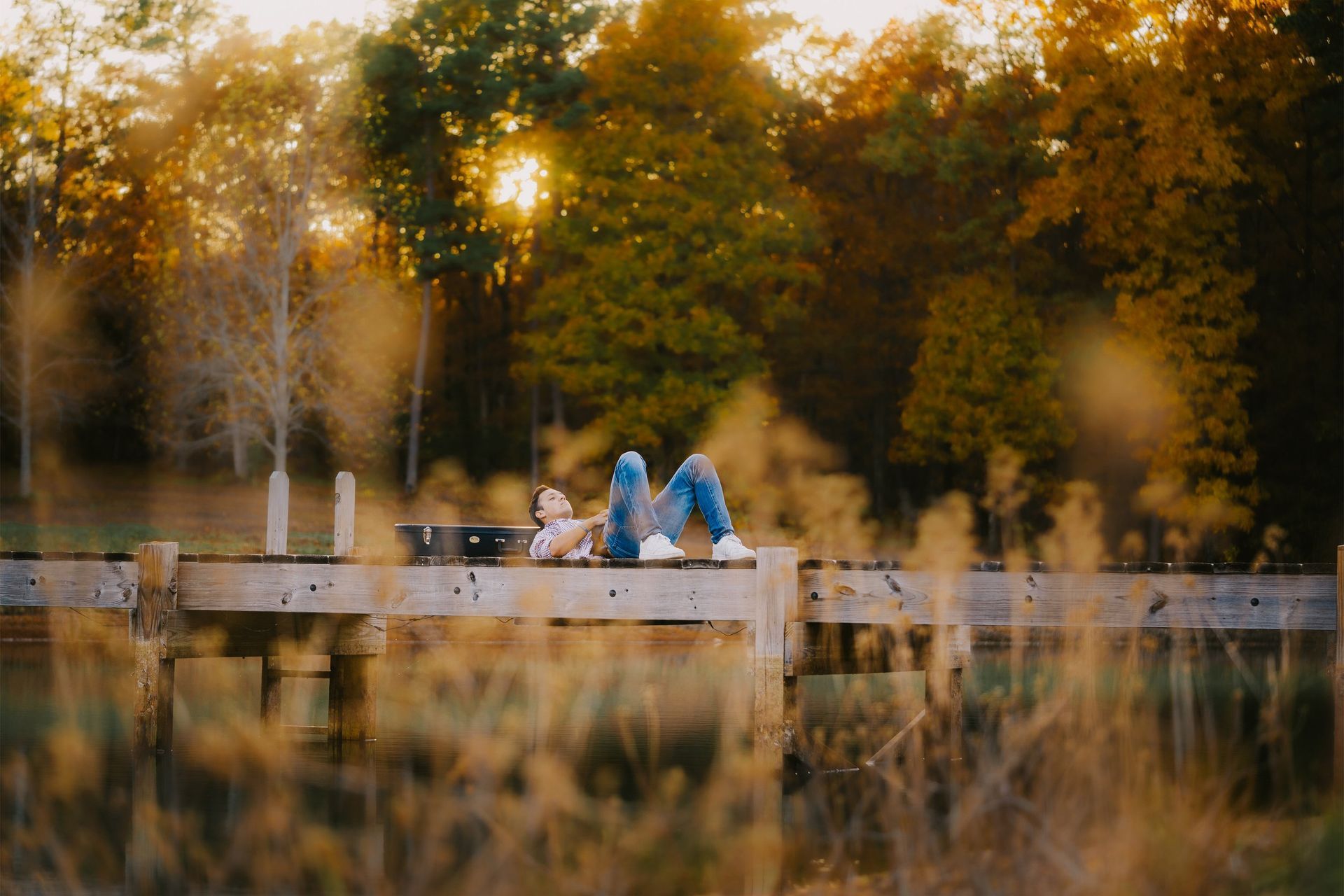 A person is laying on a wooden bridge in the woods.