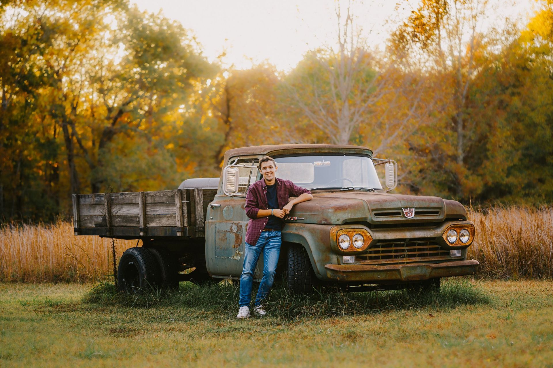 A man is leaning against an old rusty truck in a field.