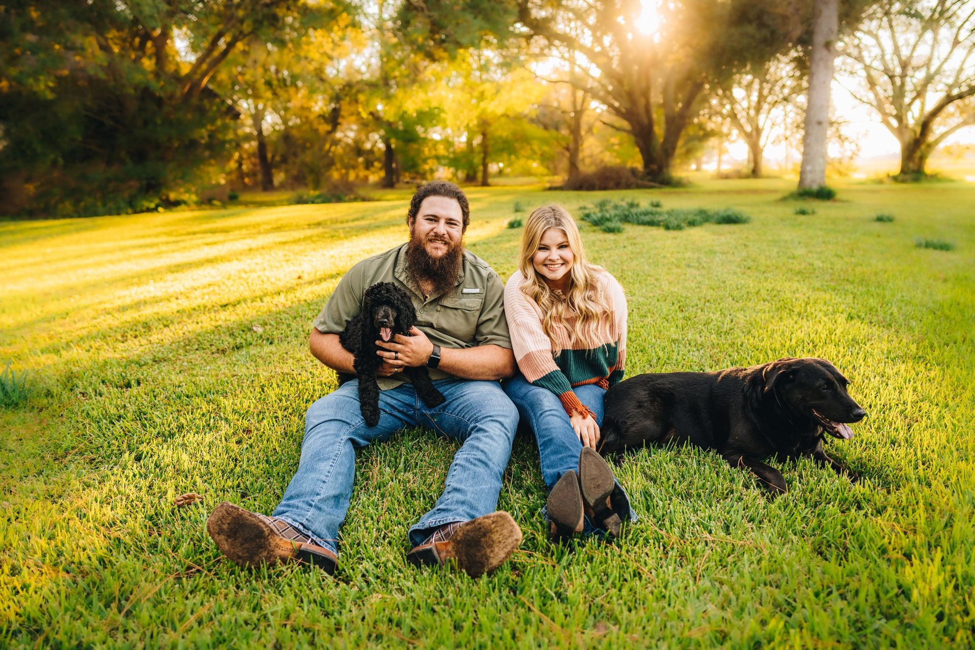 A man and a woman are sitting in the grass with their dog.