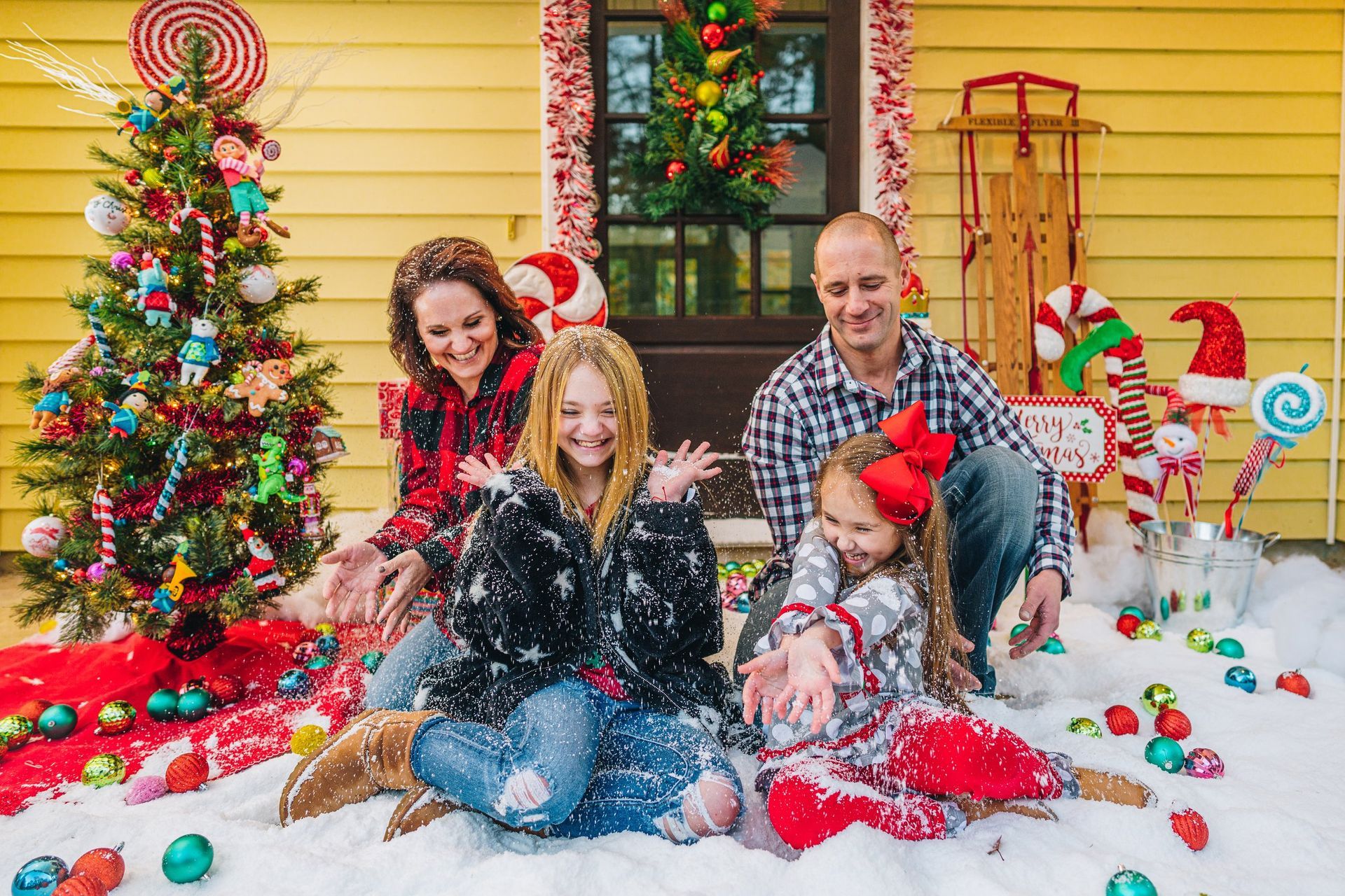 A family is playing in the snow in front of a christmas tree.