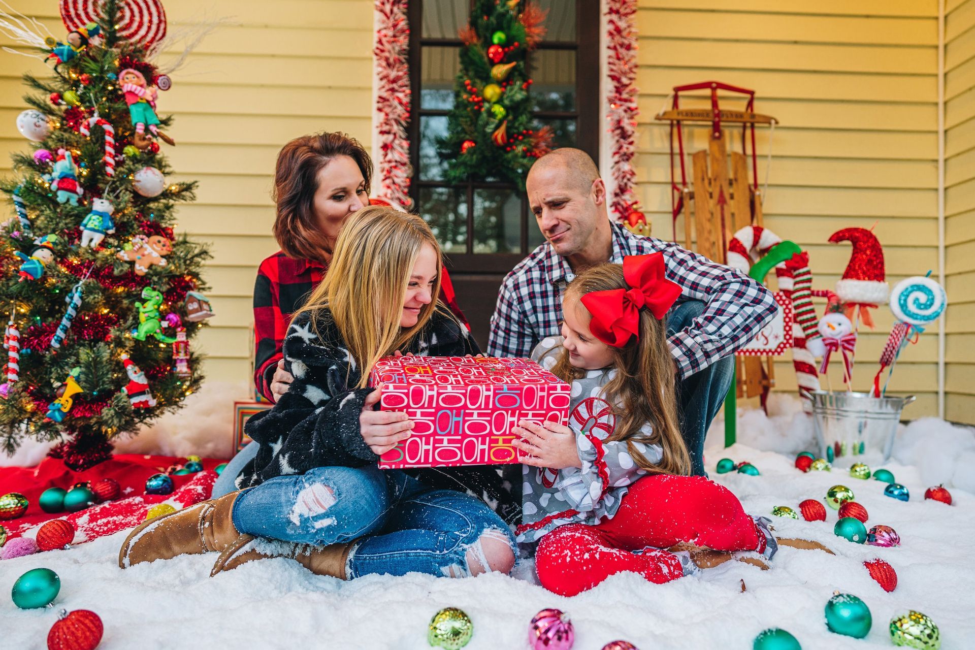A family is sitting on the porch of a house holding a christmas present.