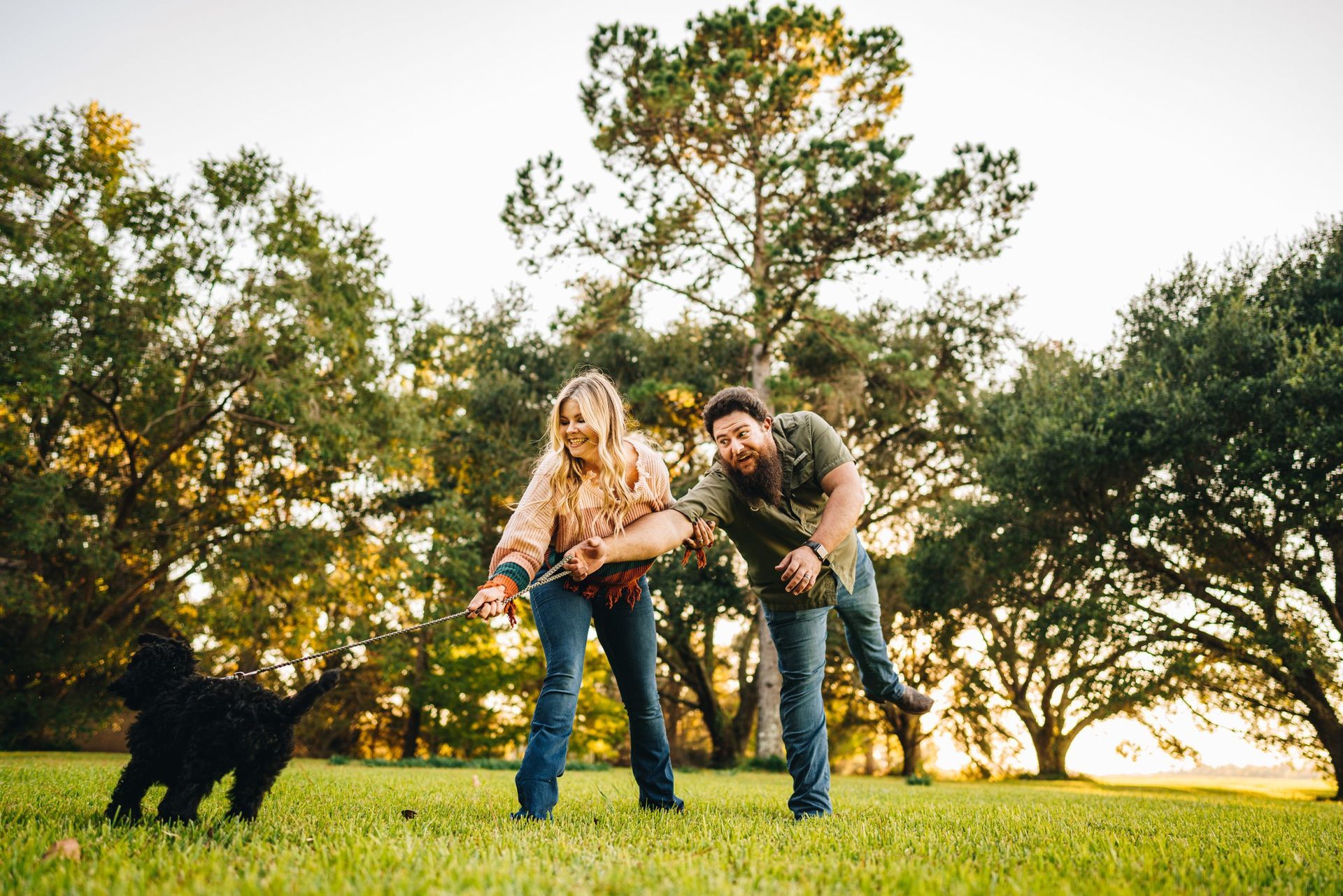 A man and a woman are playing with a black dog in a park.