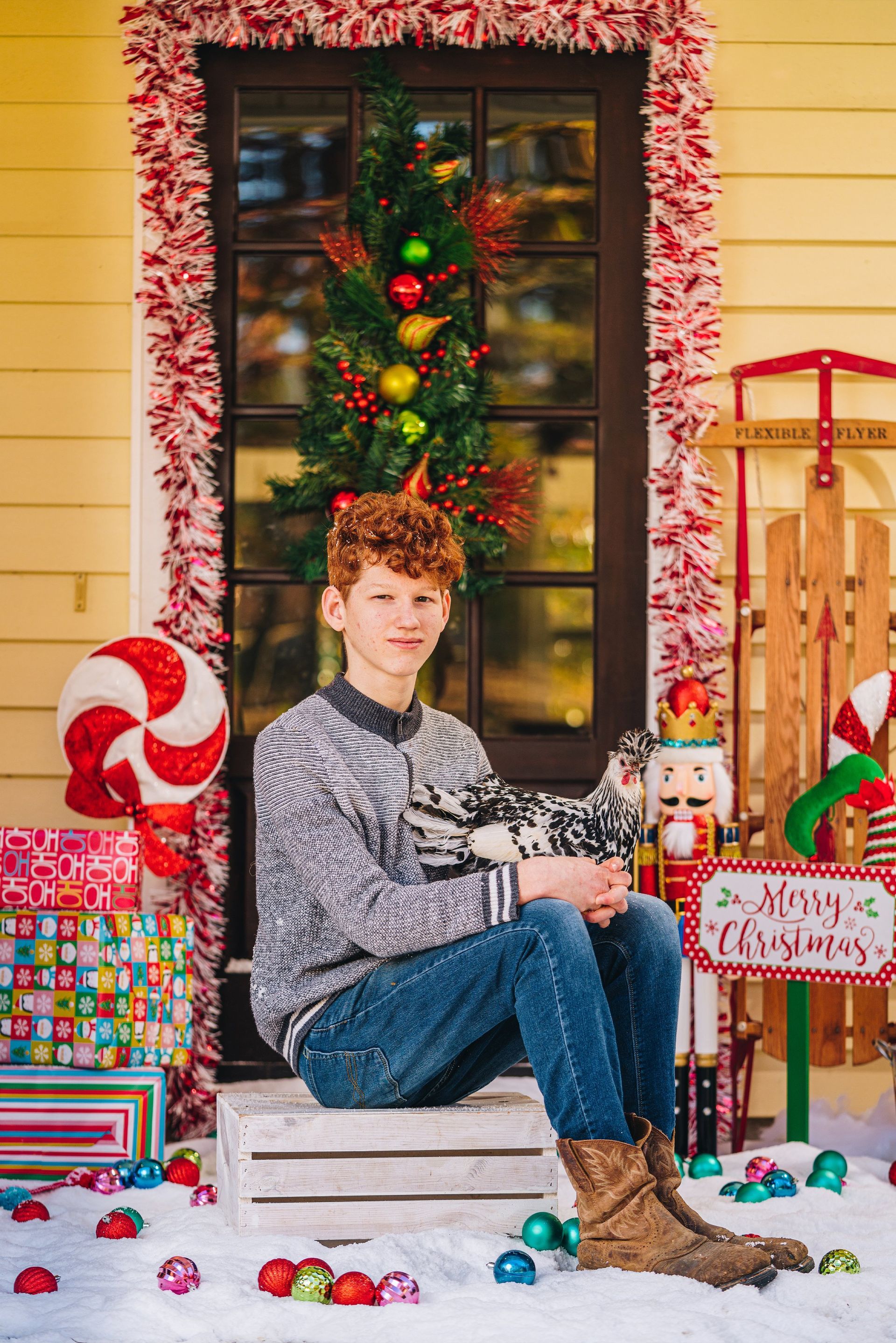 A young boy is sitting on a crate in front of a christmas tree.