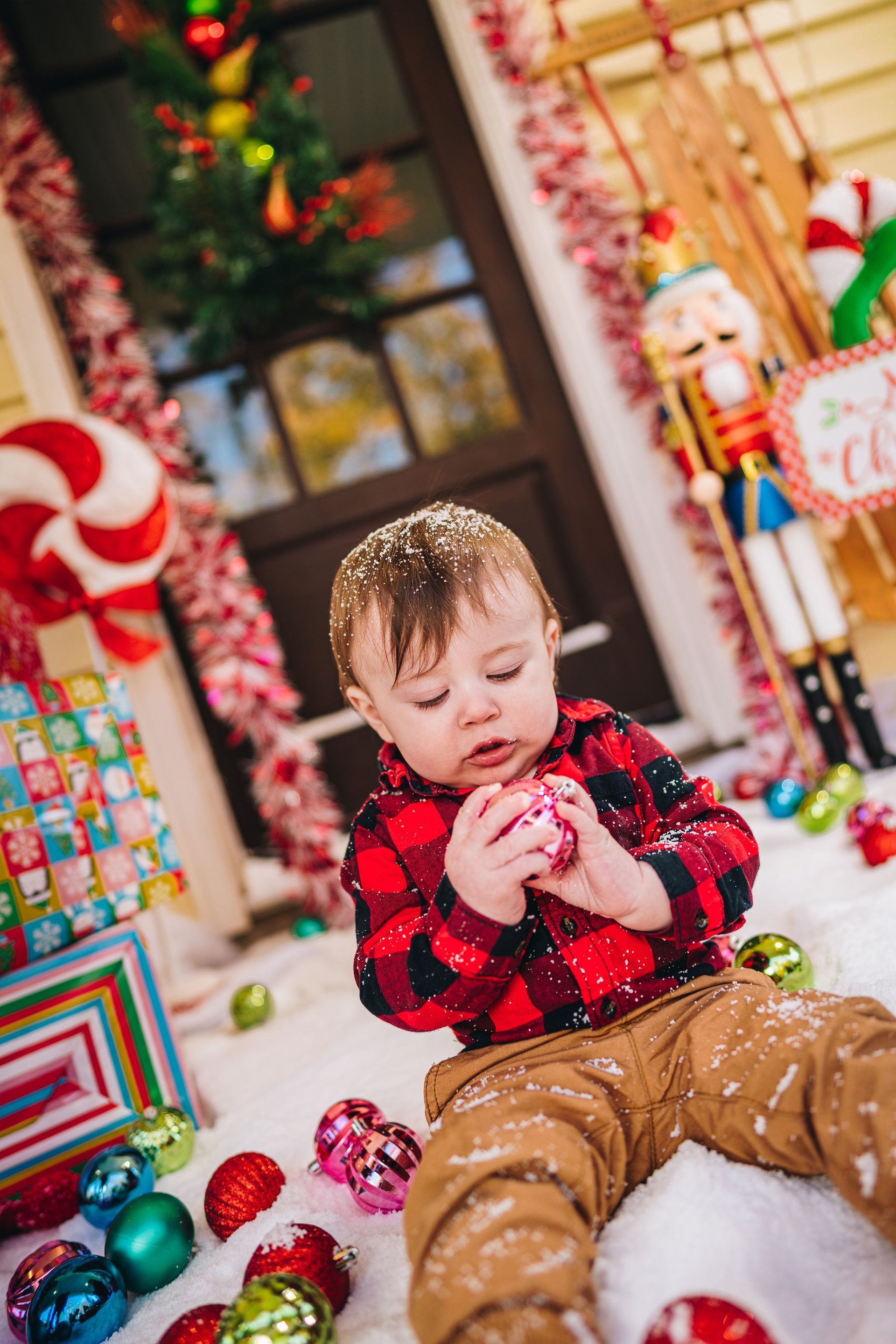 A baby is sitting in the snow holding a christmas ball.
