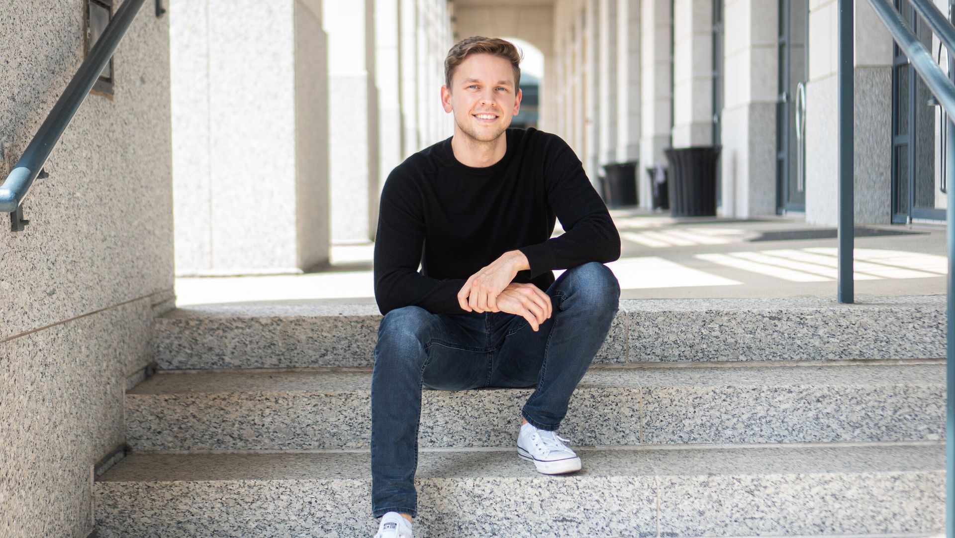 A man is sitting on a set of stairs wearing a black sweater and jeans.