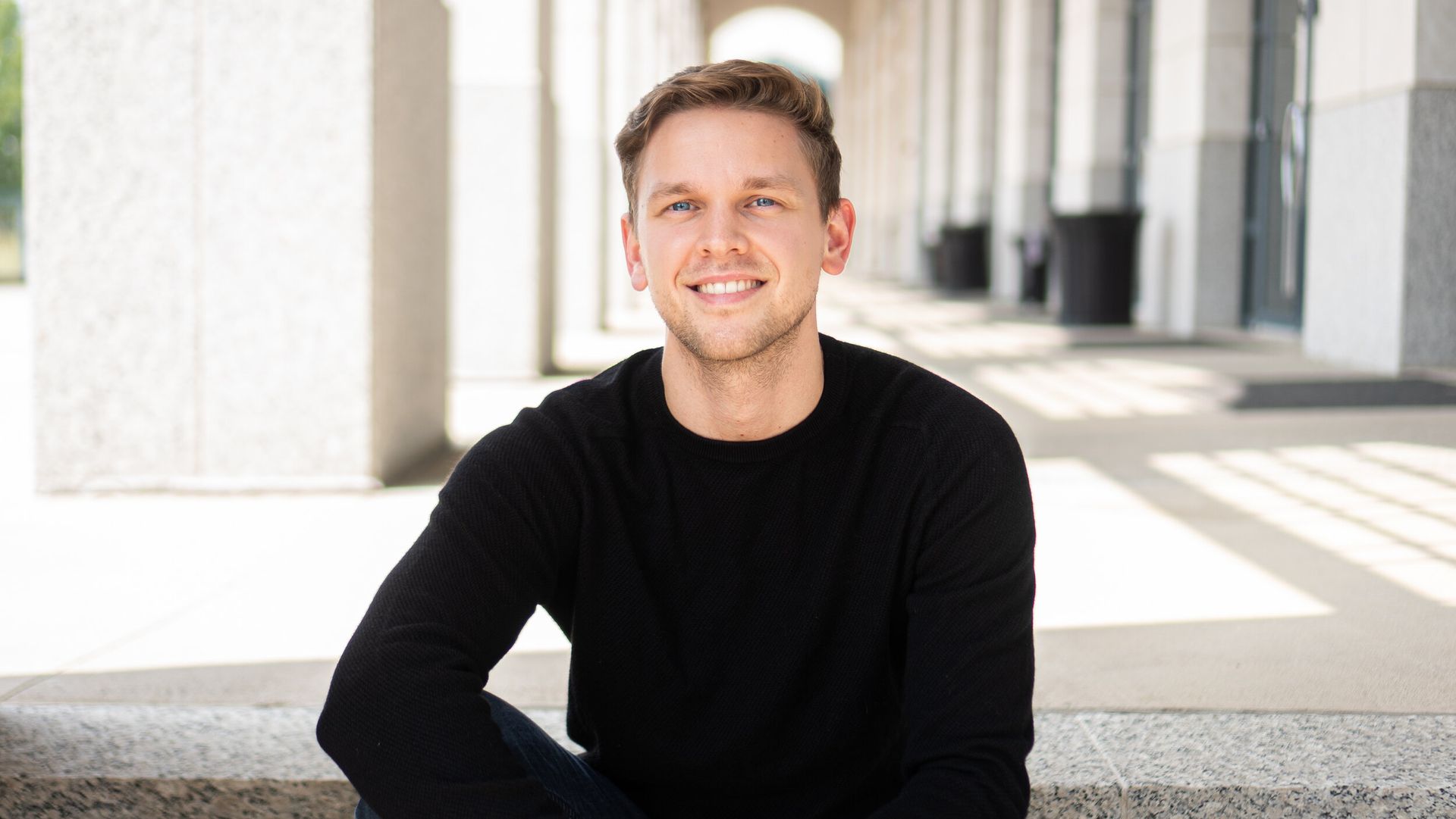 The man is wearing a black sweater and smiling for the camera.