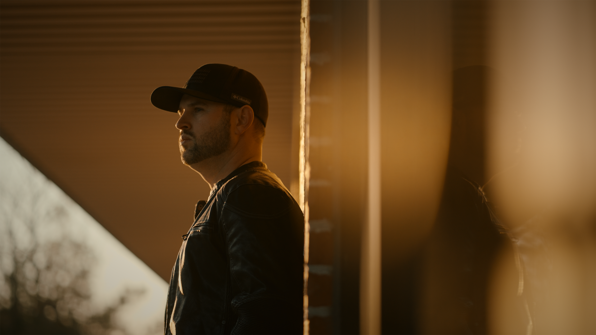 A man in a hat is leaning against a wall.