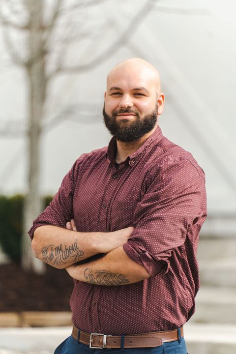 A bald man with a beard is standing with his arms crossed.