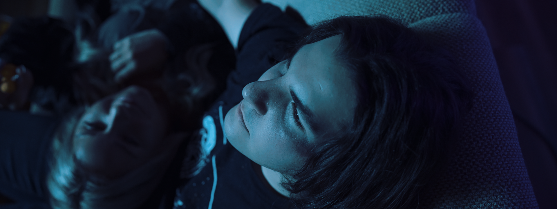 A man and a woman are laying on a bed looking at a cell phone.