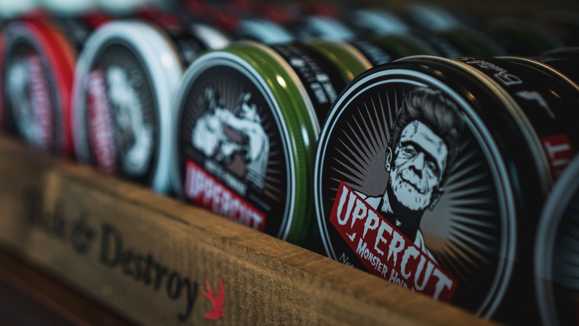 A row of cans of uppercut pomade sitting on top of a wooden shelf.