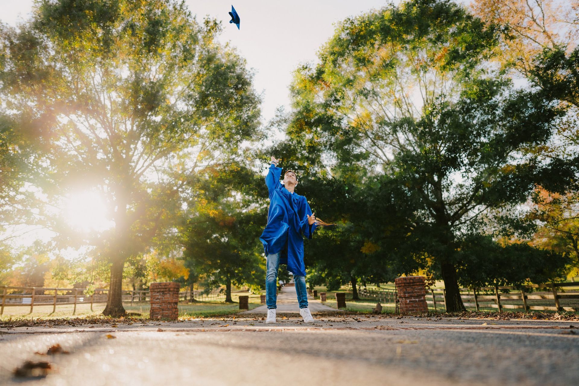 A woman in a blue gown is throwing her graduation cap in the air.