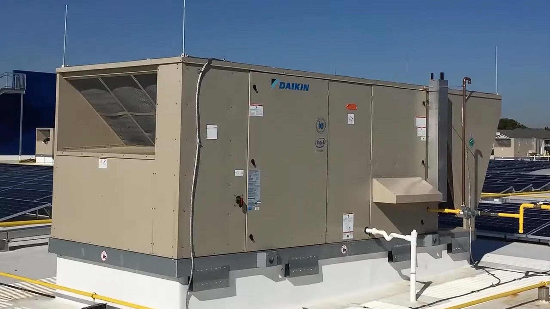 Beige rooftop HVAC unit on a snowy roof, with blue sky and yellow railings in the background