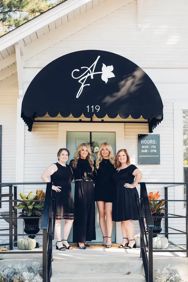 Four people in black outfits stand outside a building with a black awning and sign.