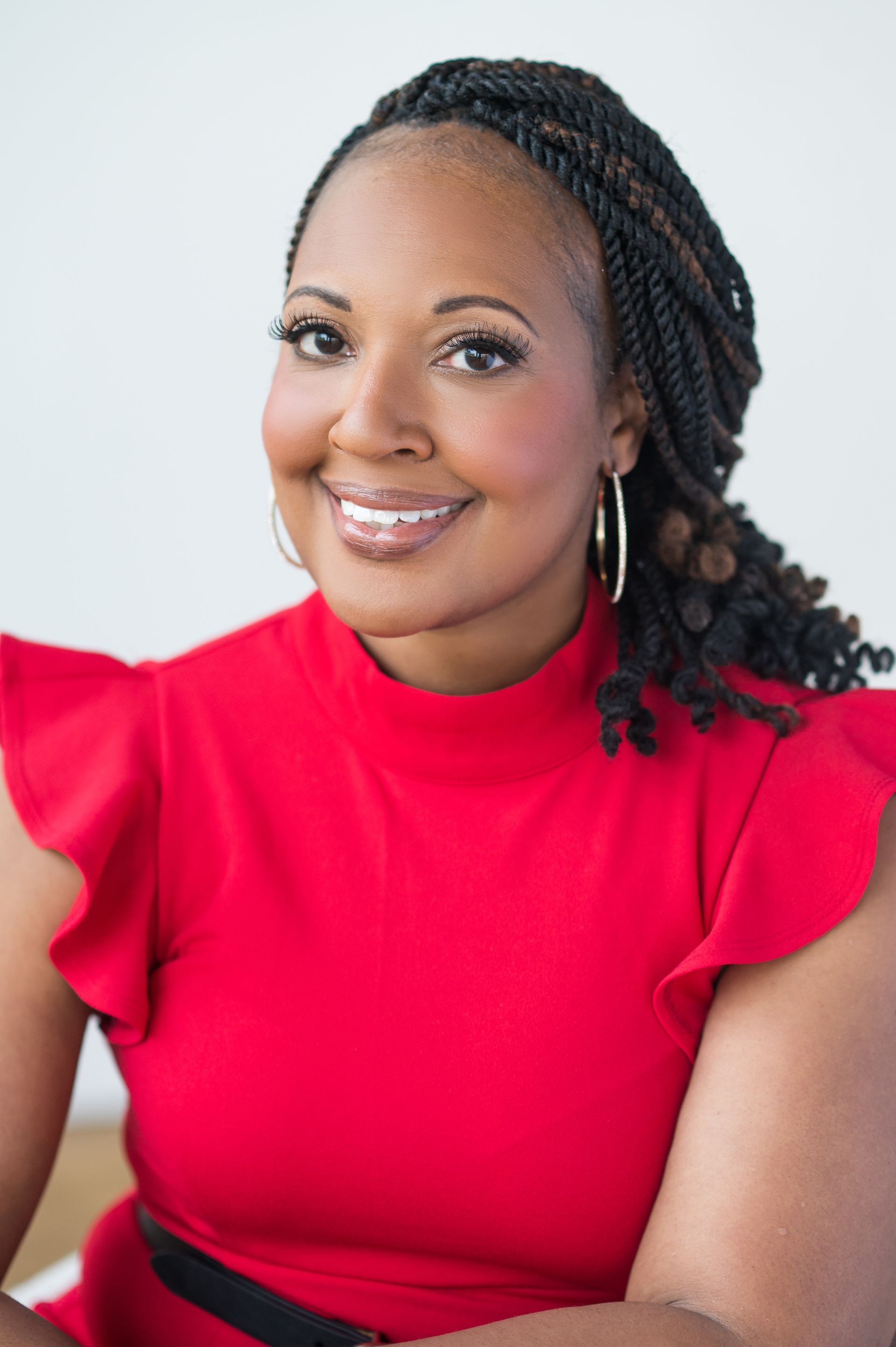 Smiling woman with long, curly brown hair wearing a light purple dress against a white background.