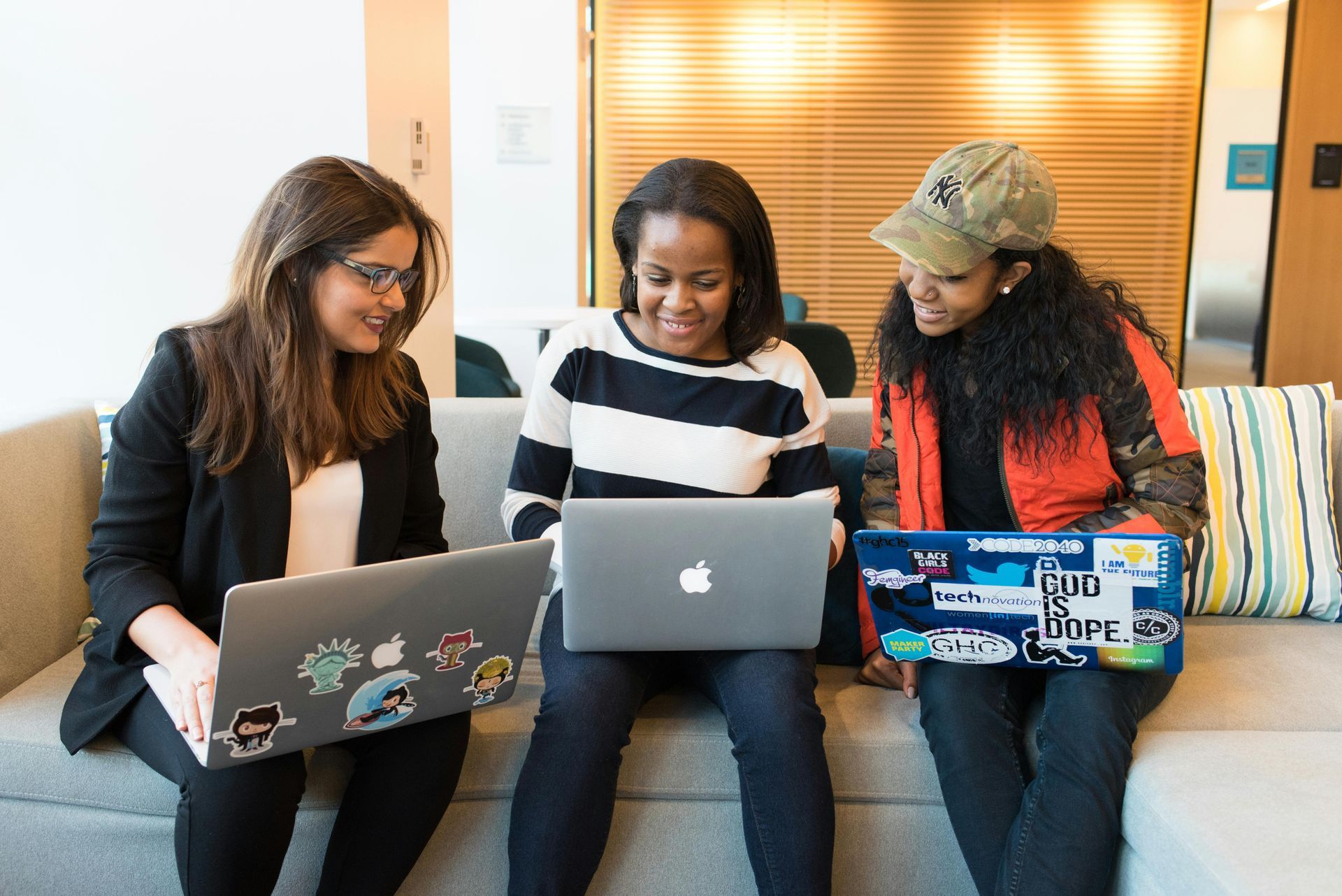 Three women sitting on a couch, working on laptops.