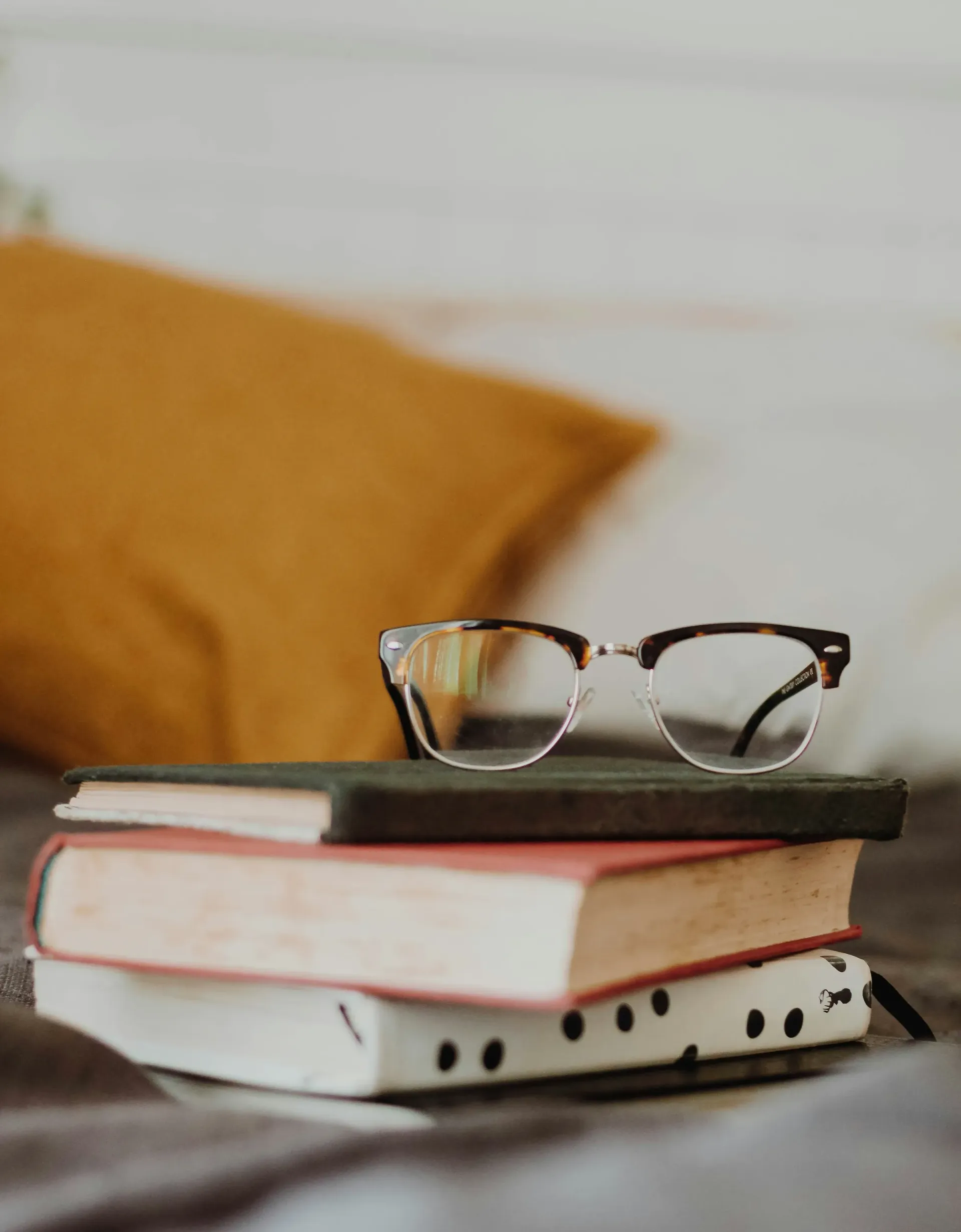 Eyeglasses resting on stacked books on a table, with a yellow pillow in the background