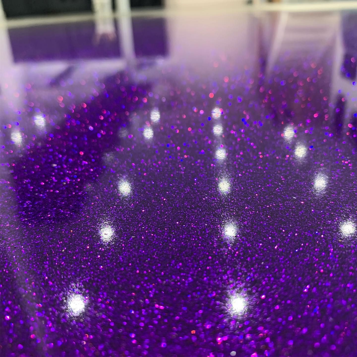 Close-up of a glossy, deep purple surface embedded with fine, sparkling glitter, reflecting small, bright point lights.