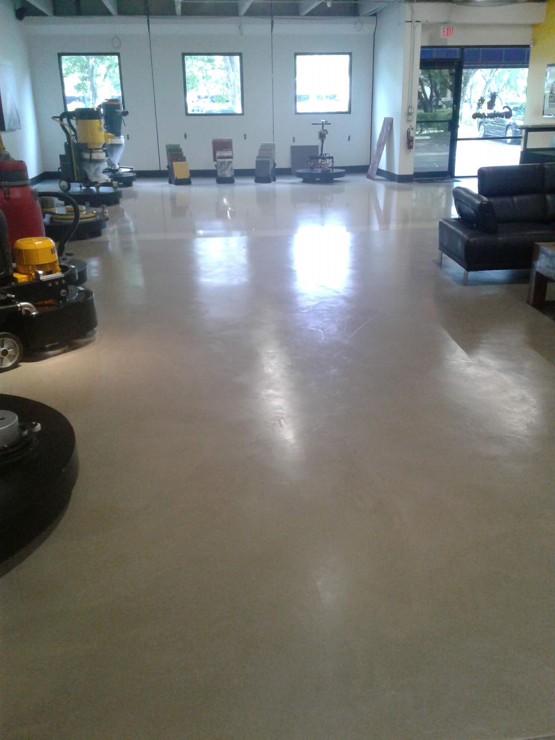 A brightly lit commercial space featuring a polished, reflective floor with floor cleaning equipment and black furniture.