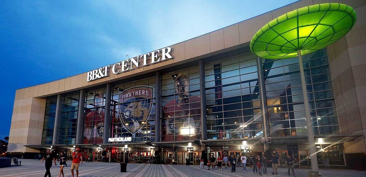 The AT&T Center arena in San Antonio at twilight, featuring a large glass facade and a prominent green outdoor sculpture.