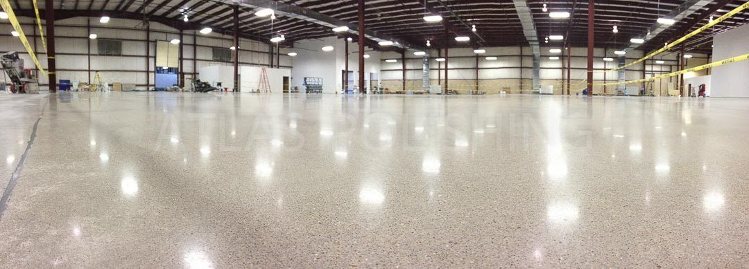 A wide, panoramic view of a large, empty warehouse with a polished, reflective concrete floor and high ceilings.