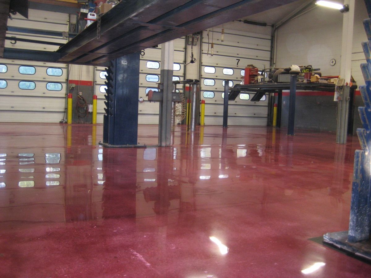 A high-gloss, deep red epoxy floor in a spacious automotive service bay with overhead lifts and numbered garage doors.