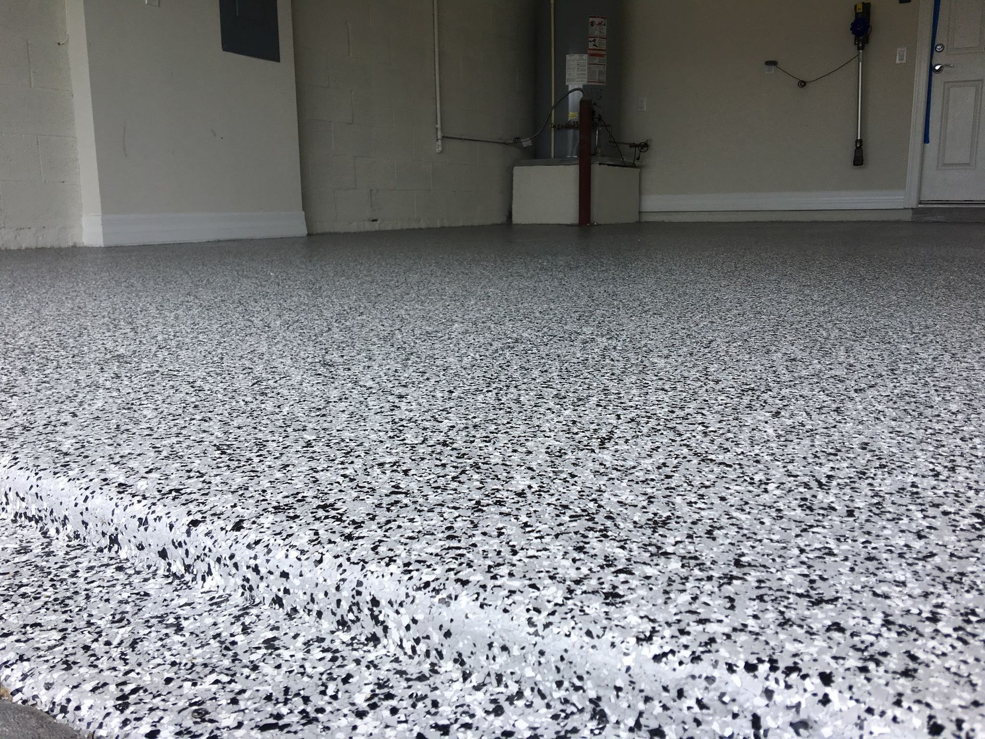 A residential garage with a light gray epoxy floor coating featuring a speckled black, white, and gray flake finish.