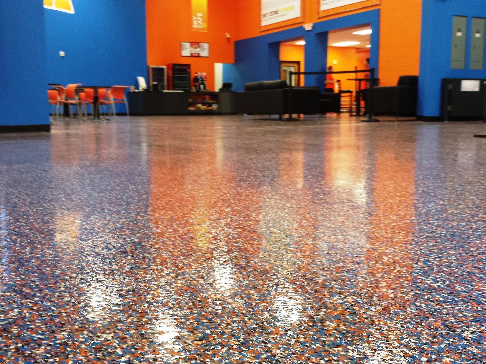 High-gloss, multi-colored speckled epoxy floor in a brightly lit, modern commercial space with orange and blue walls.