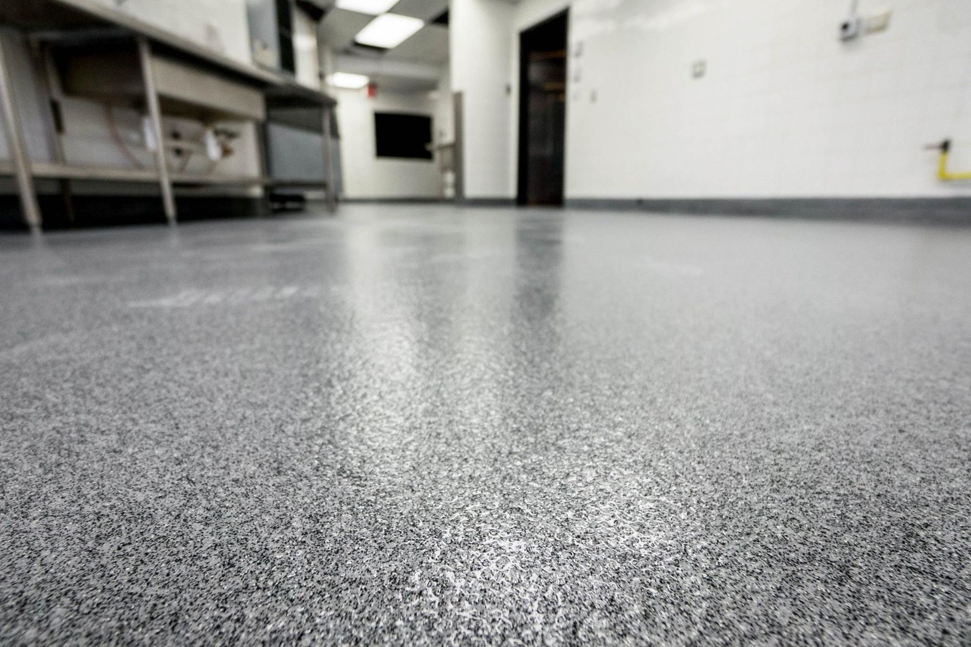 A low-angle view of a grey and black speckled epoxy floor in a commercial kitchen or hallway.