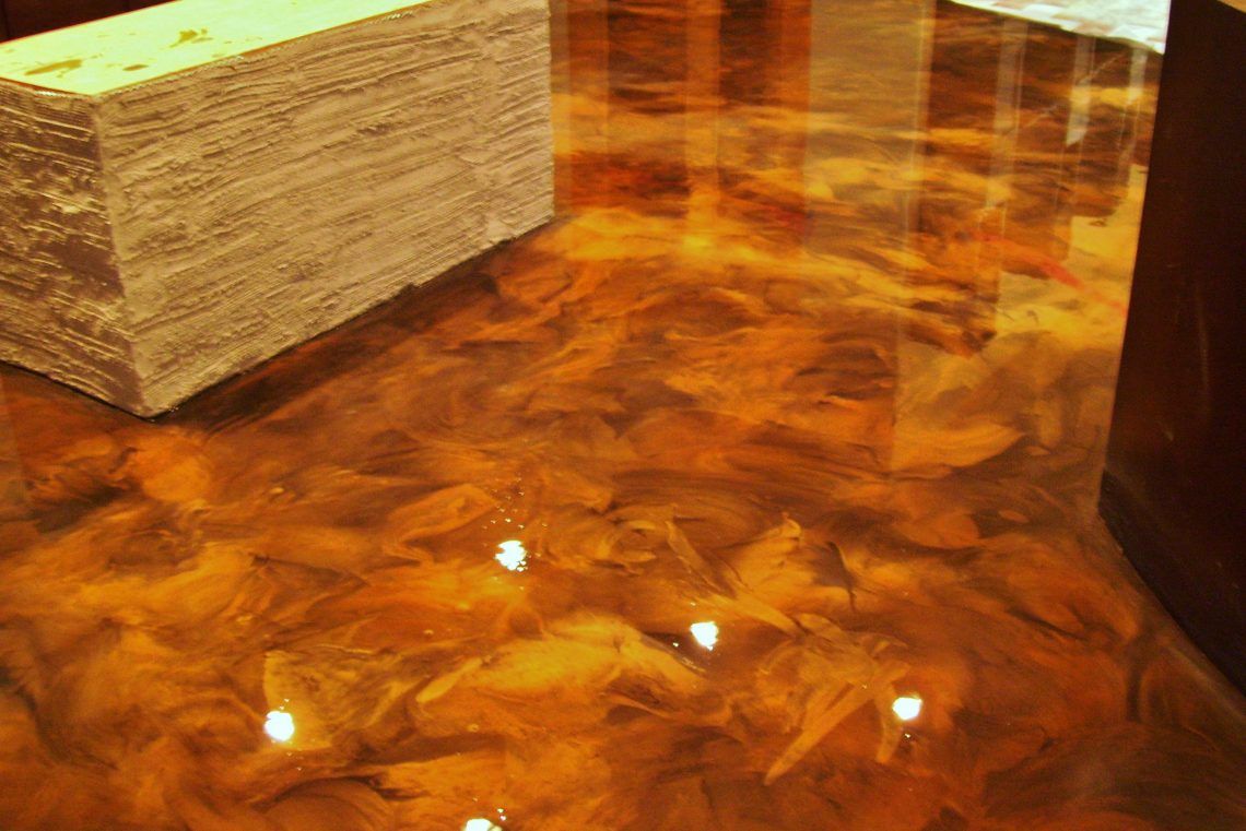 A high-gloss, swirling metallic copper epoxy floor with a textured, light-colored rectangular block on the left.