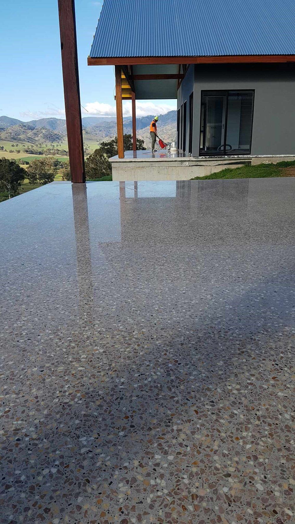 Polished concrete terrace overlooking a scenic valley with a person working on the house porch in the distance.