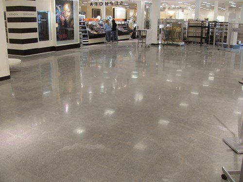 A spacious retail store interior with highly polished, reflective concrete flooring and soft overhead lighting.