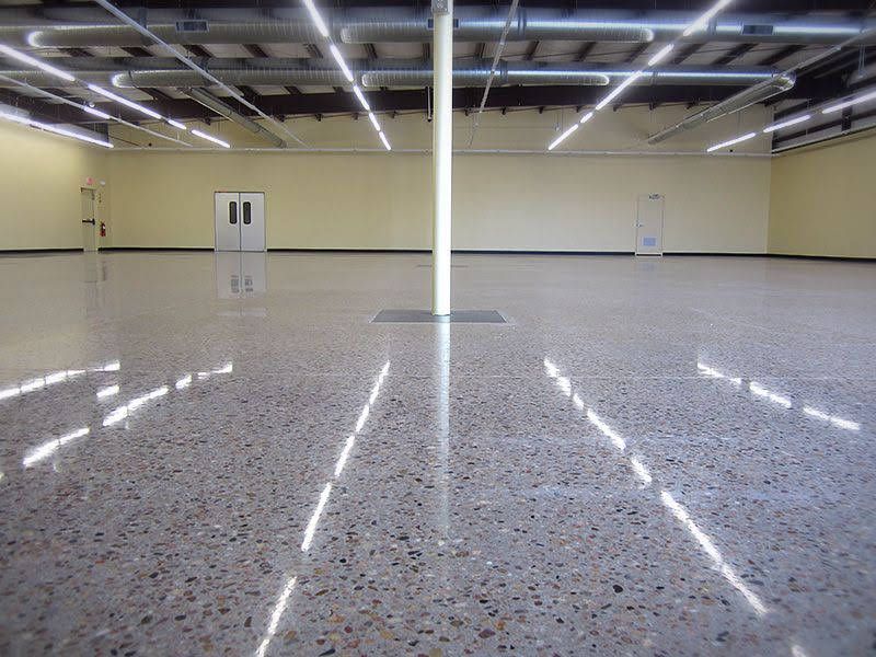 Wide view of a large, empty commercial space with polished speckled concrete floors and bright overhead lighting.