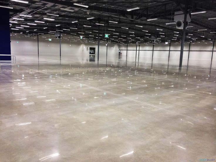 A wide-angle, interior view of a large, empty, modern warehouse space with polished concrete floors and bright lighting.