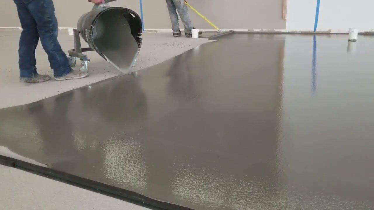 Workers pouring self-leveling concrete onto a floor surface to create a smooth, flat foundation.