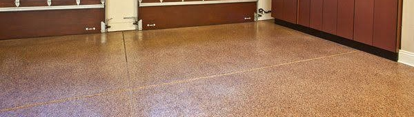 A garage floor with a brown speckled epoxy finish, featuring a visible seam and brown cabinets in the background.