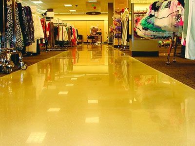 A low-angle view of a shiny, light-yellow floor in a clothing store, with racks of clothes on either side.