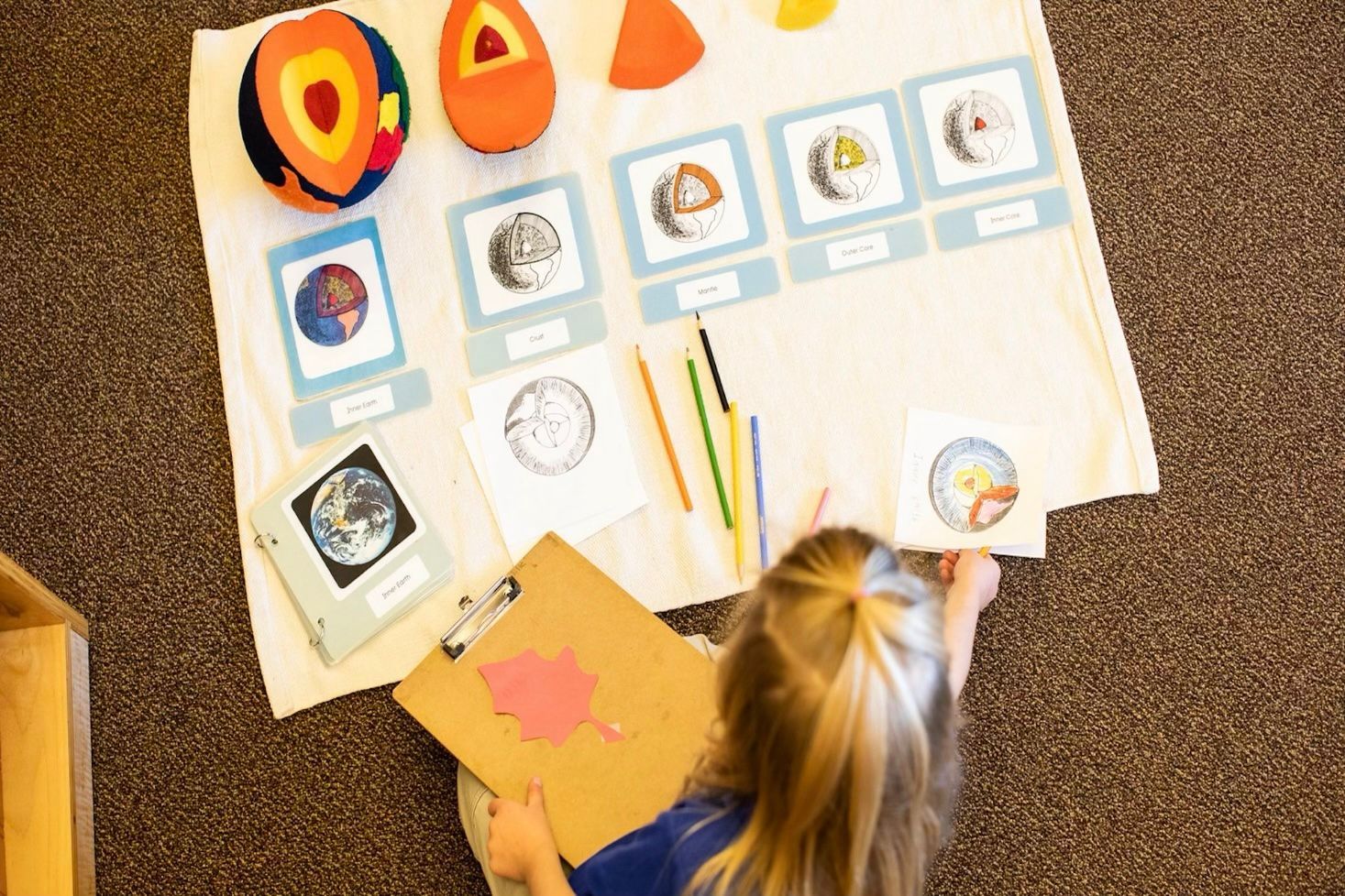 Child working on a colorful craft project with paper, crayons, and art cards on the floor