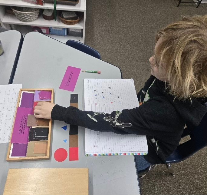 Person at desk using geometric shapes. Notebook and cards present.