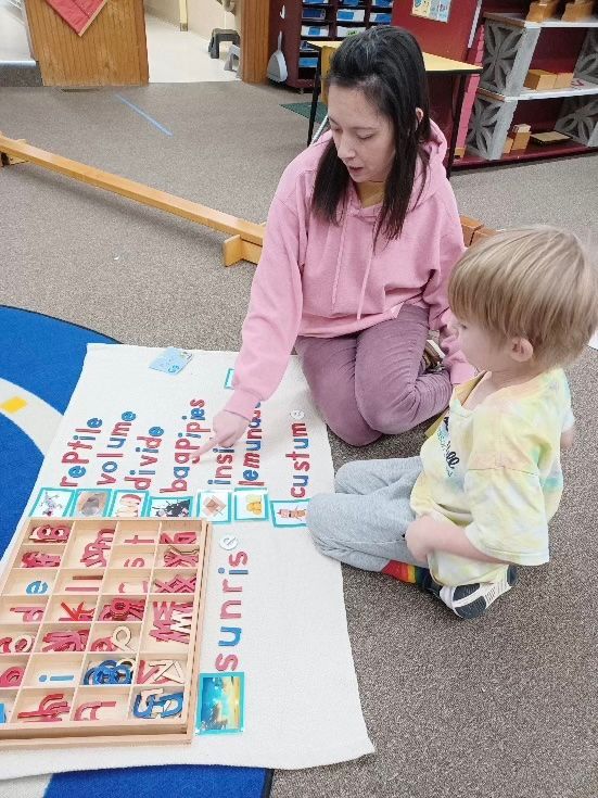 Woman and child working with an alphabet. The woman points to a word, and the child looks on.