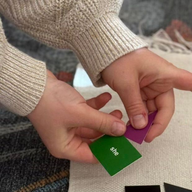 Child using color-coded word cards to explore pronouns in a Montessori language activity.